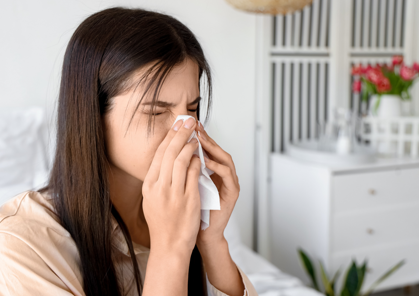 Woman sneezing into a tissue while sitting on her bed